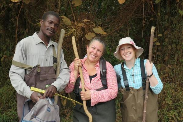 Smiling at the camera are two white women and a black man wearing brown waders and holding walking sticks