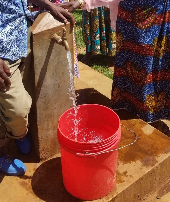 People standing at a faucet of water outdoor filling a red bucket of water