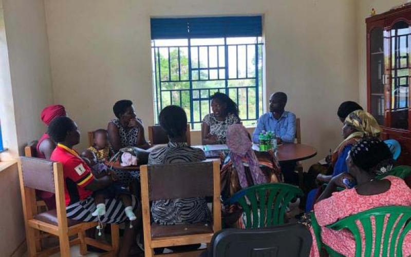 A group of men and women and a couple children sitting indoors around a table having a discussion