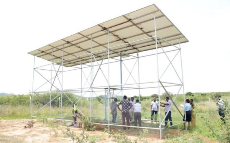 People stand under a solar panel located in a field.