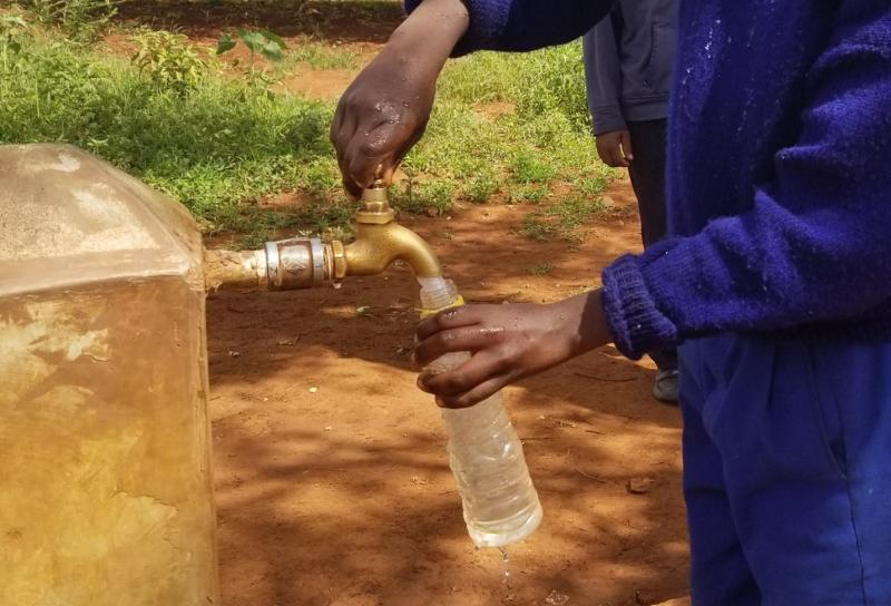 someone in blue standing, filling a bottle of water at a faucet outdoor 