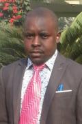 Bahati Hakimu, a black man with a bald head, wearing a suit with a pink tie