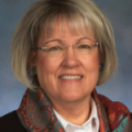 Sally Miller, a white woman with a blonde bob haircut and bang, wearing glasses and a patterned scarf