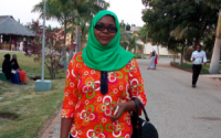 Zaina Hussein, a Black woman in a headscarf, a colorful dress, and sunglasses