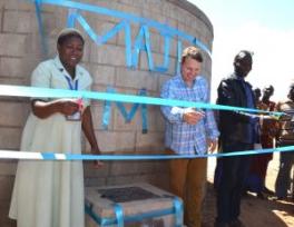 Three people with scissors posed behind a blue ribbon with a rainwater collection system behind them