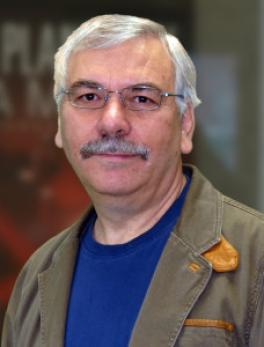 Frank Schwartz, a white man with white hair, a moustache, and glasses. He is wearing a blue t-shirt and a canvas jacket.