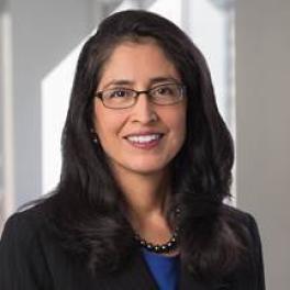 Hilary Tompkins, a Navajo woman with long black hair and glasses, wearing a black blazer and a blue shirt