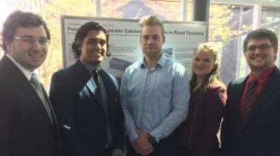 Five young people in business formal wear standing in front of a research poster