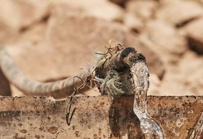 Clear water streaming through a hose. The hose is brown, wrapped with twine, and hooked to a flat piece of metal