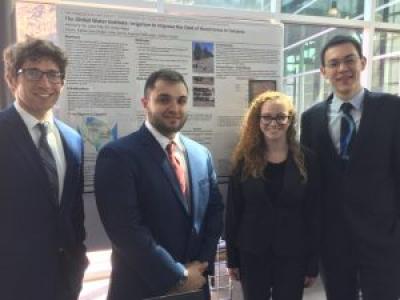 Four young people in business formal wear standing in front of a research poster