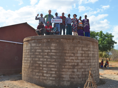 A dozen people standing on top of a rainwater harvester made of brick. One of them is holding a sign that says "GO BUCKS"