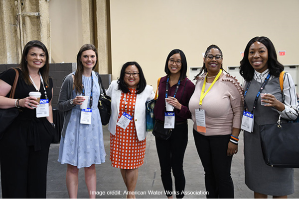 A group of 6 women in business attire with name tag lanyards posing indoor