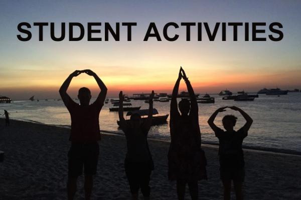 Four people standing on a beach at sunset making the "O-H-I-O" arm gesture shape
