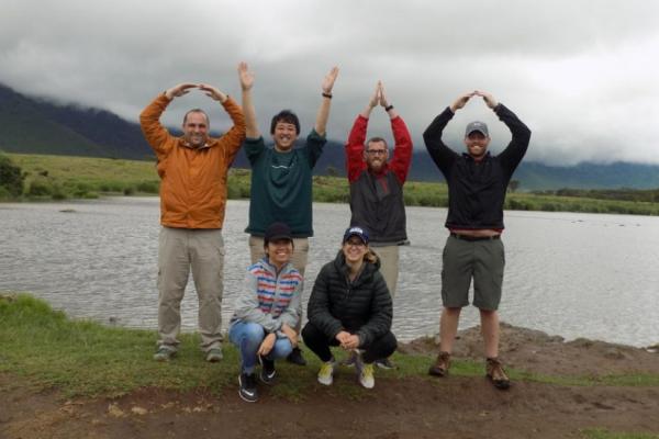 Six people in front of a lake. Two are kneeled in front. Four are in the O-H-I-O arm pose