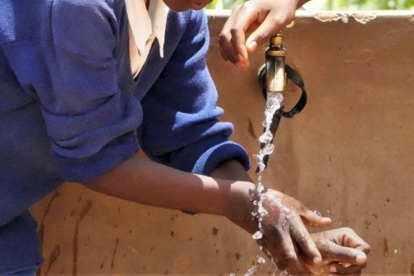 A Black person washing their hands in an outdoor facet
