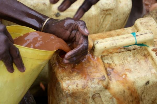 Orange water being poured from a bucket into a dirty plastic water canister..