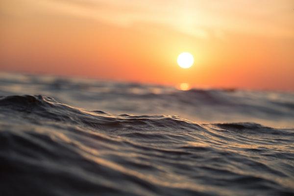 surface level view of open water with calm waves and orange sun and sky