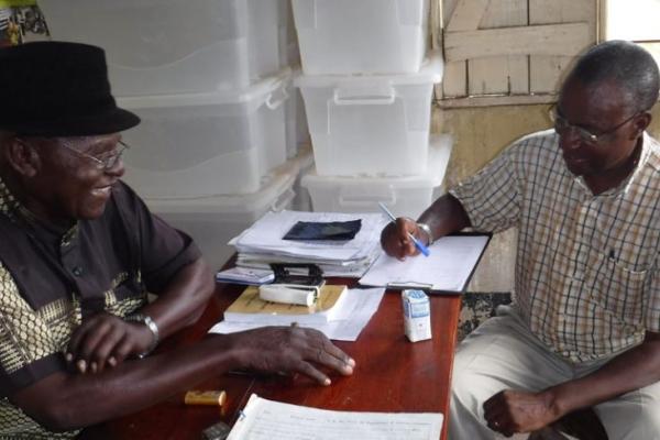 To older Black men at a table, working on files and smiling