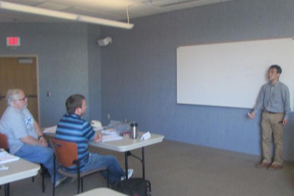 Three people, one standing in front of a white board, the other two sitting at a table