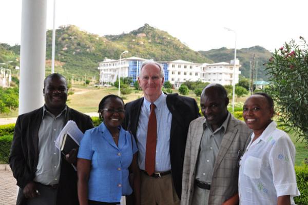 Mixed race, mixed gender group of people in business wearing standing outside with a large white building and a lush, green hill behind them