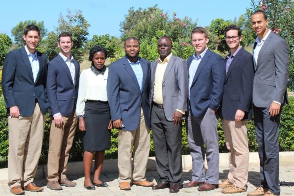 A mixed race, mixed gender group of people in business formal wear standing on a brick path in front of some foliage
