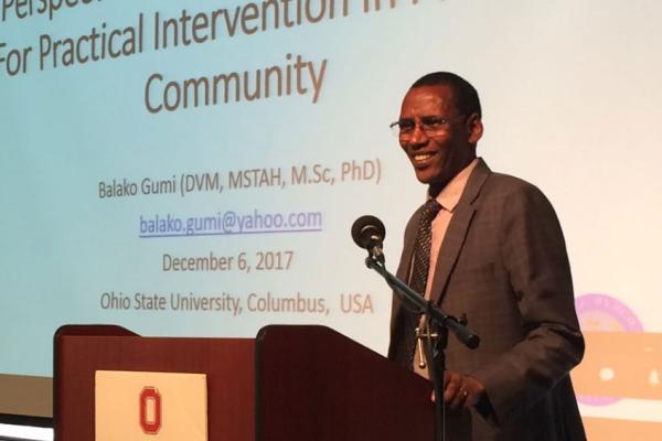 Balako Gumi, a Black man with short cropped hair wearing a suit, giving a presentation