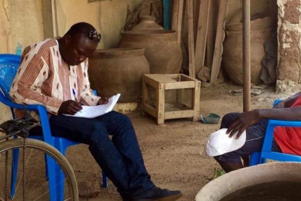 Two black men sitting in plastic chairs across from each other. One is reading a document.