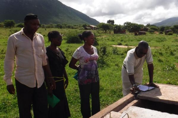 A group of Black people performing field work in a lush green field with a mountain looming in the background