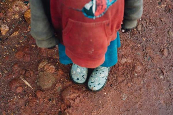 A child in a sweatshirt, shorts, and space-themed rainboots standing in red mud