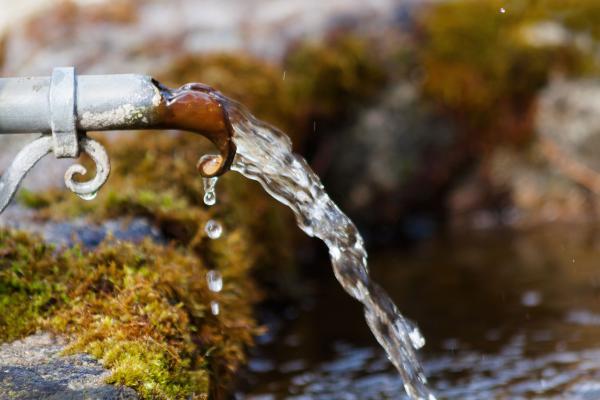 A stream of water pouring from a metal faucet into a moss-covered stone pool