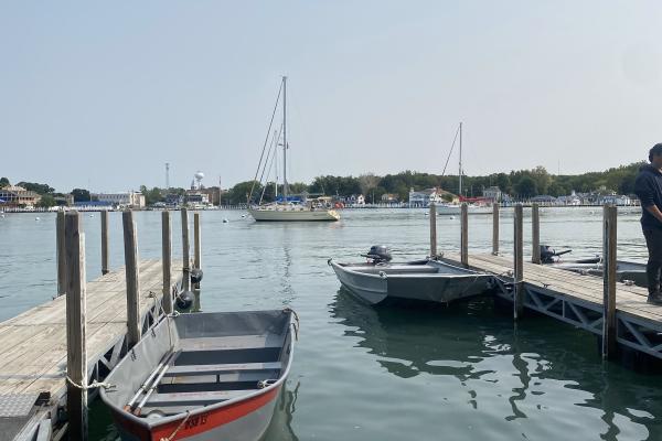 Two boats docked to two docks on the water and another boat and land in the disitance