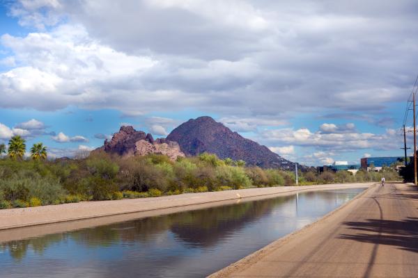 A canal in Phoenix with a background of blue skies, white clouds, mountains and vegetation.
