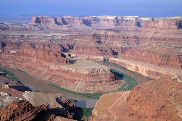 A curved river in the carved red rocks of a deep, massive canyon stretching as far as you can see.