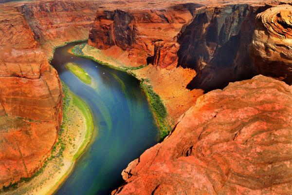 A Blue green river with algea in a red canyon with white skies.