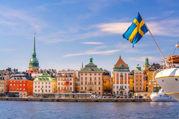 View of Stockholm's picturesque waterfront with colorful buildings and a Swedish flag fluttering on a boat.