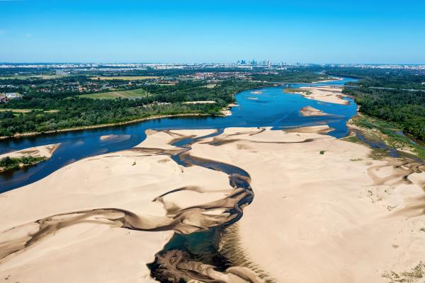 Dry riverbed with a small flowing river with vegetation and a city scape in a distance.